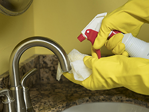 Closeup of gloved hands holding spray bottle and cleaning sink.
