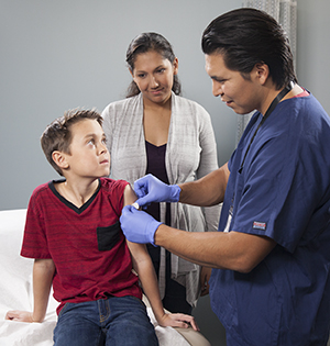 Healthcare provider giving boy injection in arm while woman looks on.