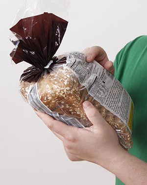 Closeup of man's hands holding bag of bread, pointing at nutrition label.