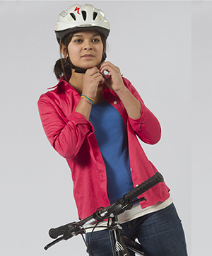 Teenaged girl on bicycle, putting on helmet.