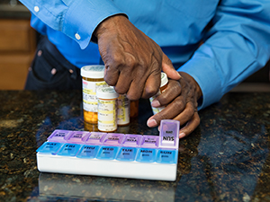 Closeup of man's hands filling pill organizer with medications.
