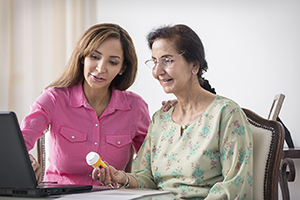 Dos mujeres mirando un frasco de medicamento y una computadora portátil.